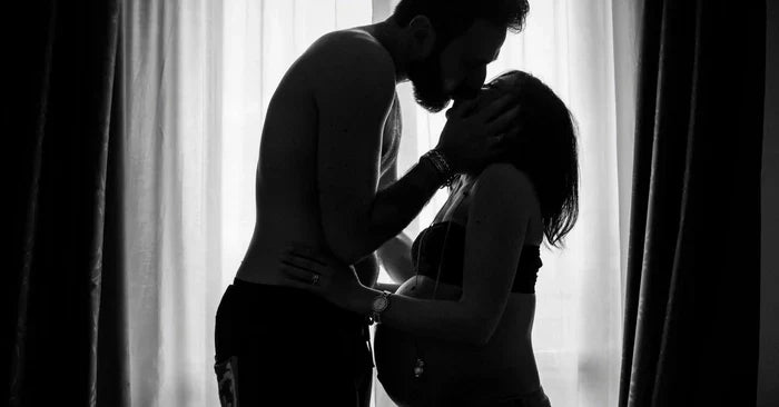 Man kissing a pregnant woman in front of the window in B&W
